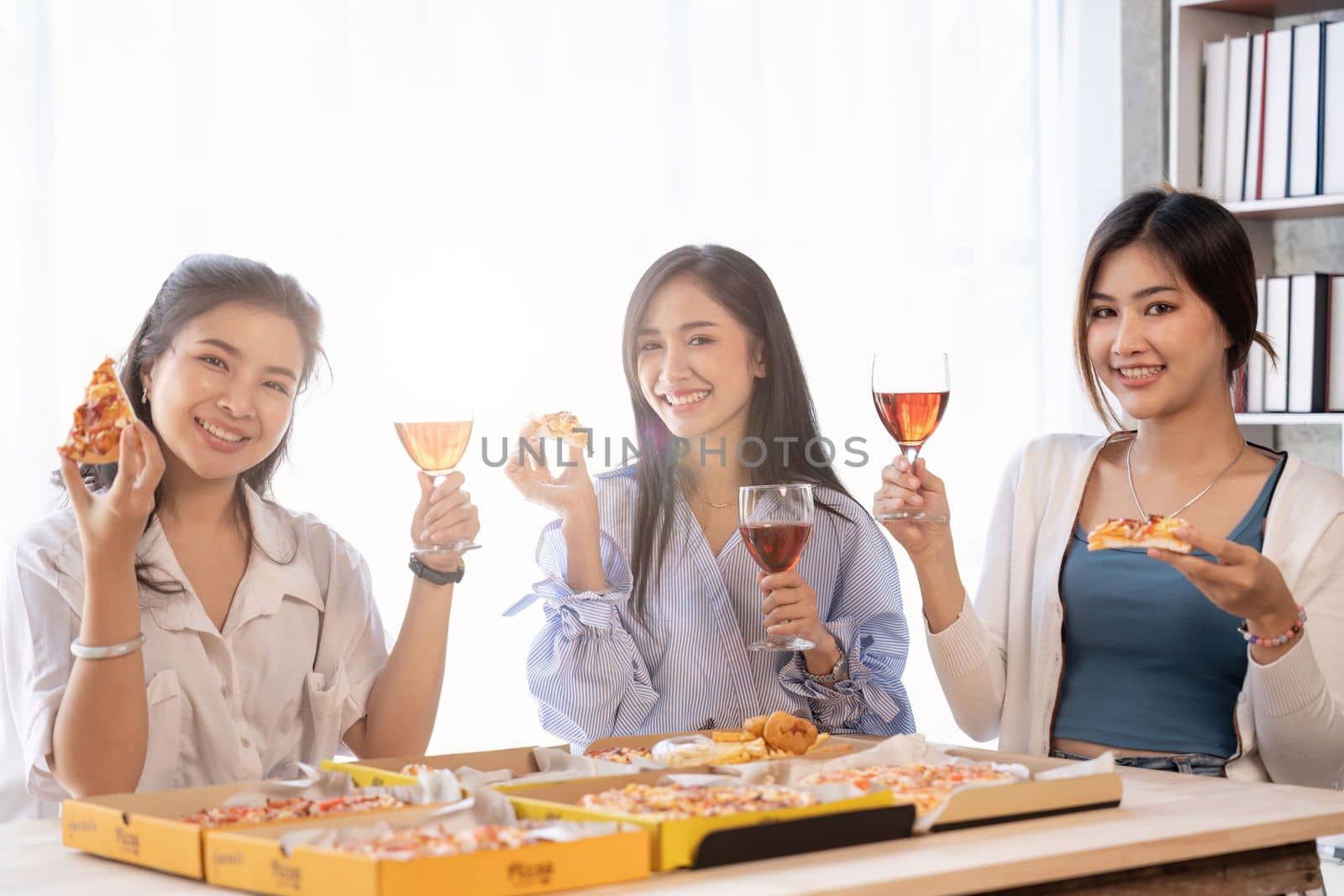 Group of Asian friends gather to celebrate Christmas with champagne and eating pizza at home. Joy of holiday party with friends or colleague concept.