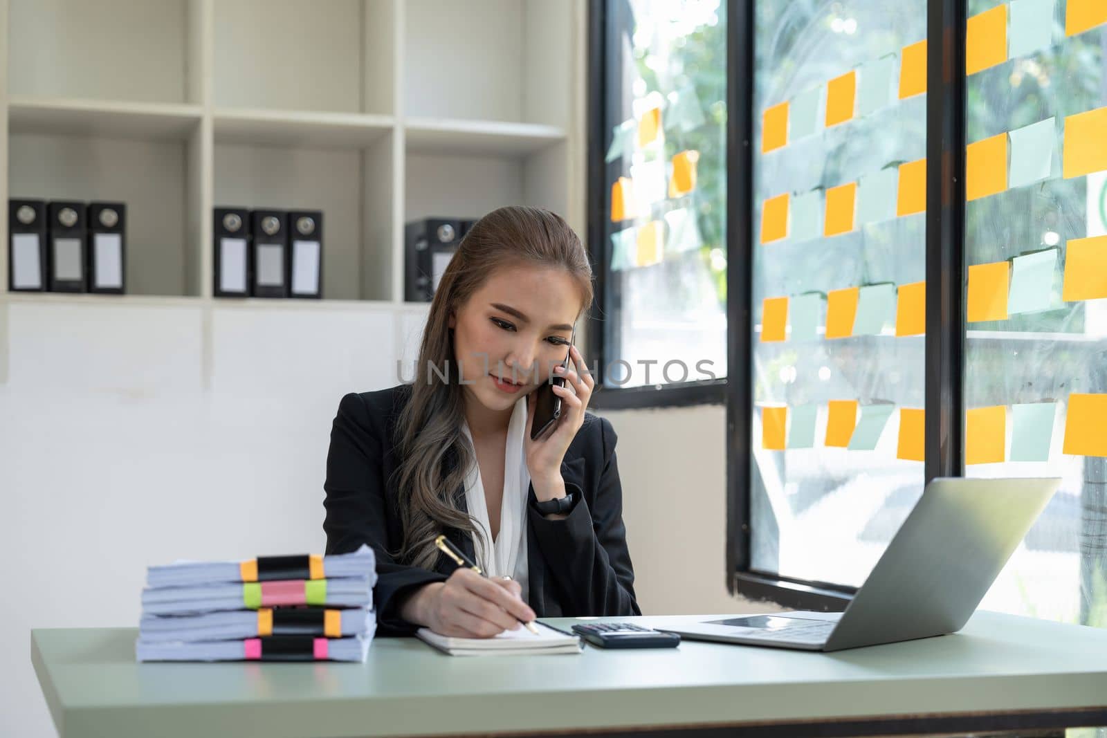 Portrait business accountant asian woman calling on phone and taking notes.