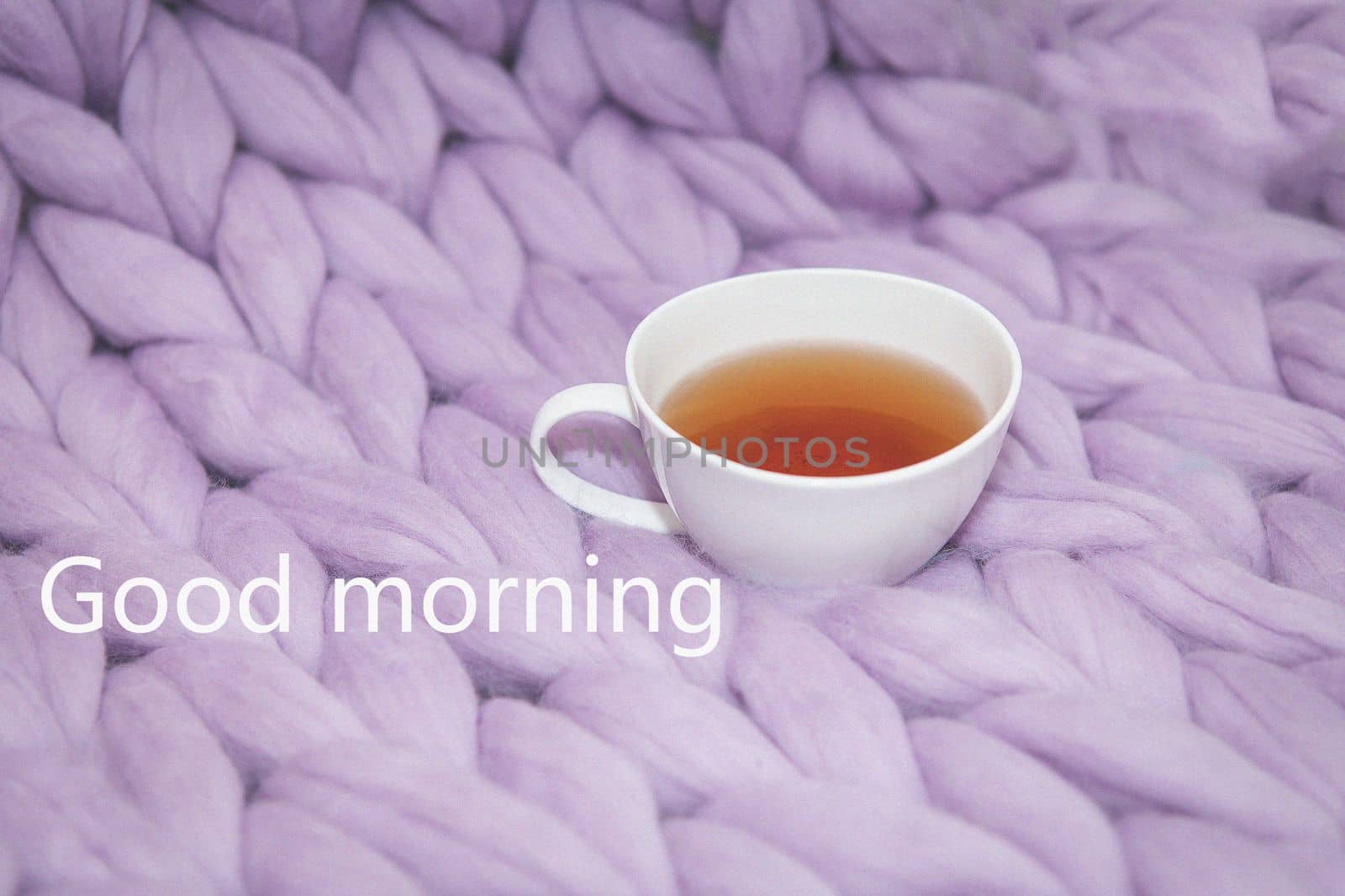 The concept of coziness and comfort is a pink-lavender knitted blanket with a white cup of tea on it. Up close Good morning inscriptions