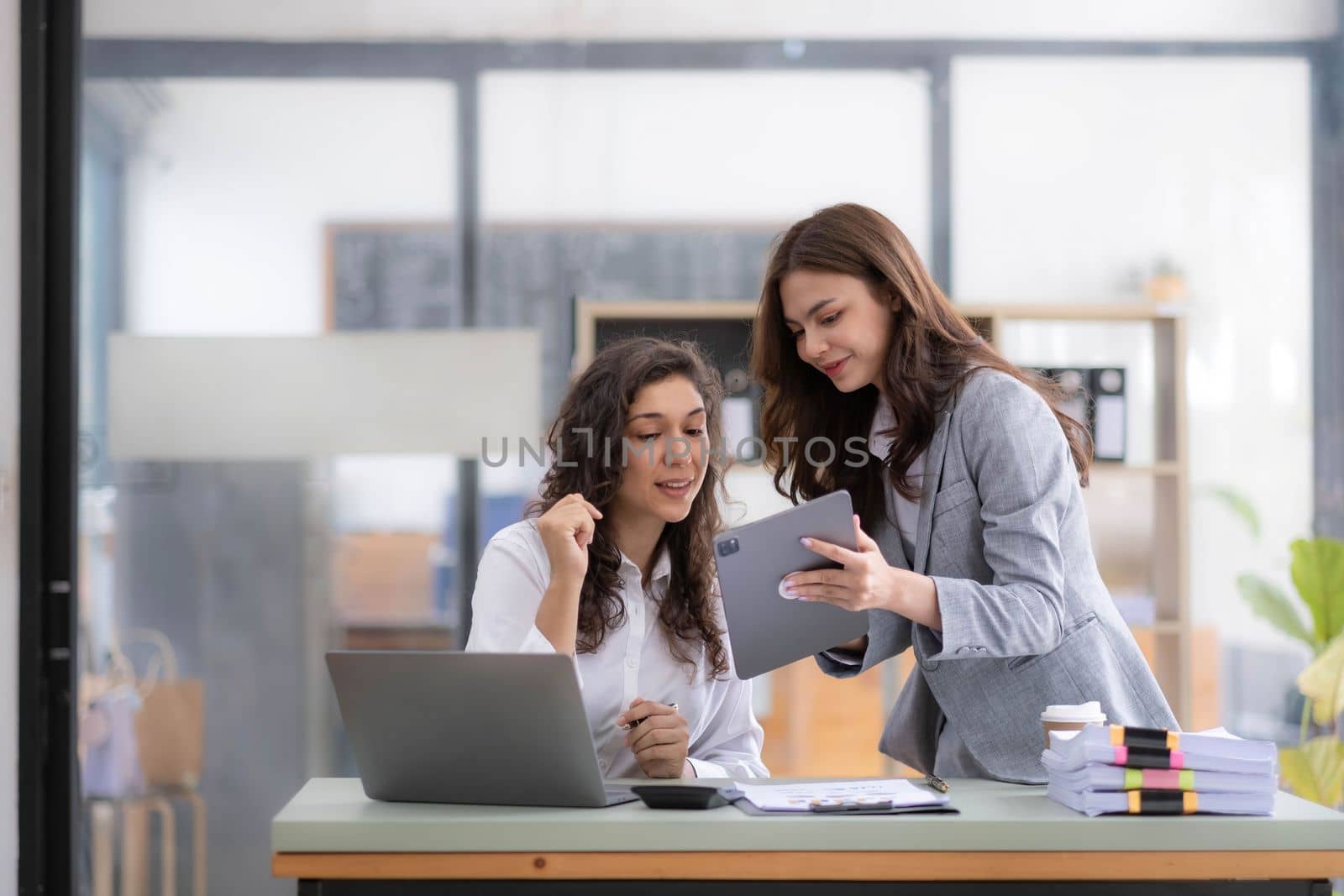 Two young Asian business woman talk, consult, discuss working with new startup project idea presentation analyze plan marketing and investment in the office..