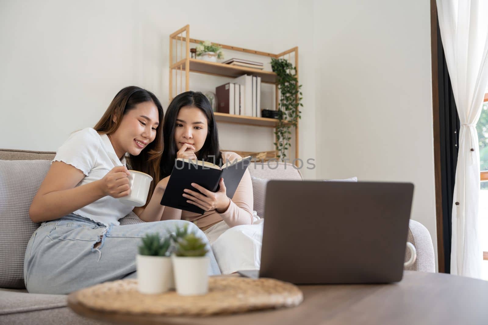 Happy two young asian girls are sitting on couch using digital tablet at home by nateemee