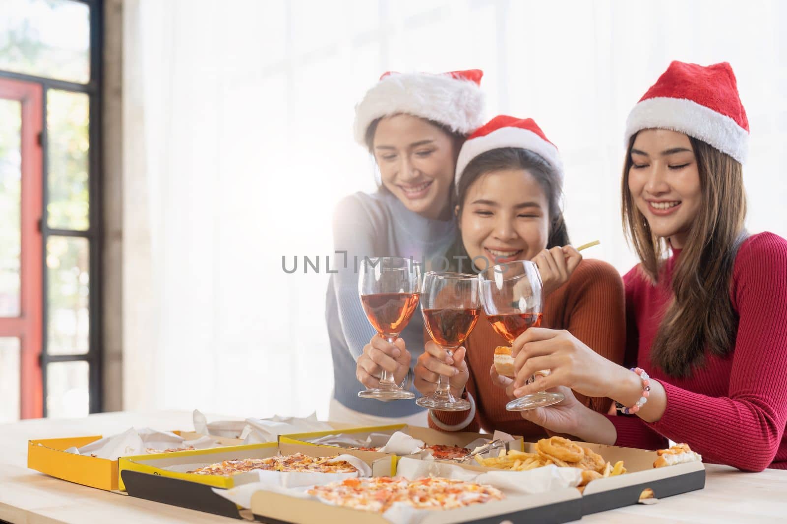 Group of Asian friends gather to celebrate Christmas with champagne and eating pizza at home. Joy of holiday party with friends or colleague concept.