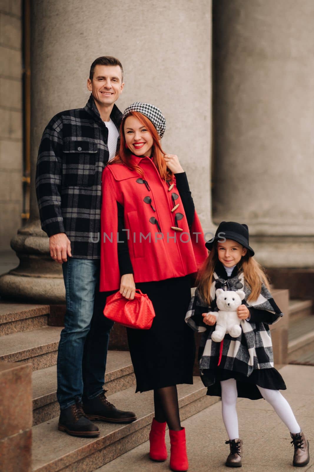 A stylish family of three is in town in the fall, and the girl with the stuffed toy is cheerful.