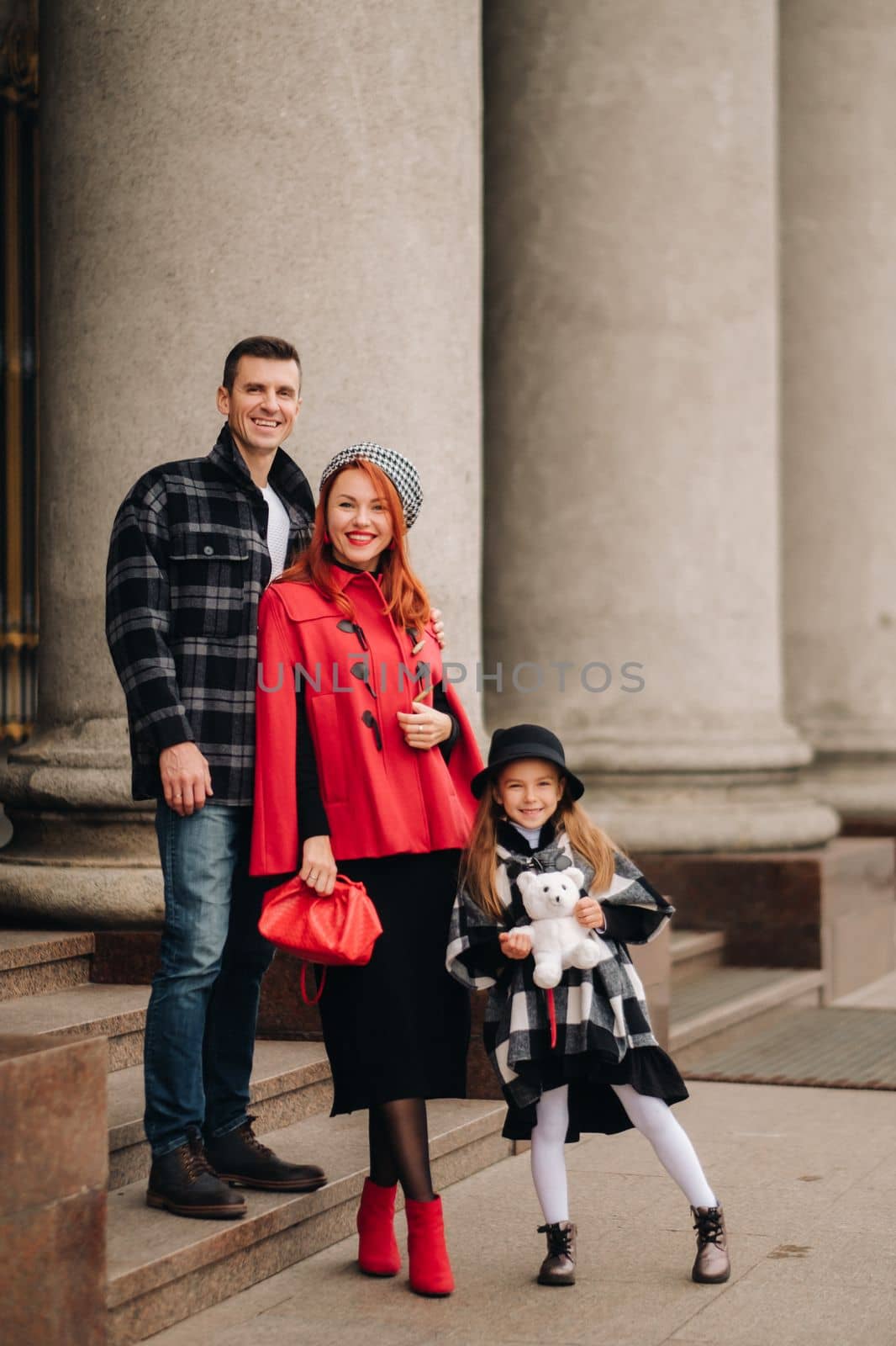 A stylish family of three is in town in the fall, and the girl with the stuffed toy is cheerful.