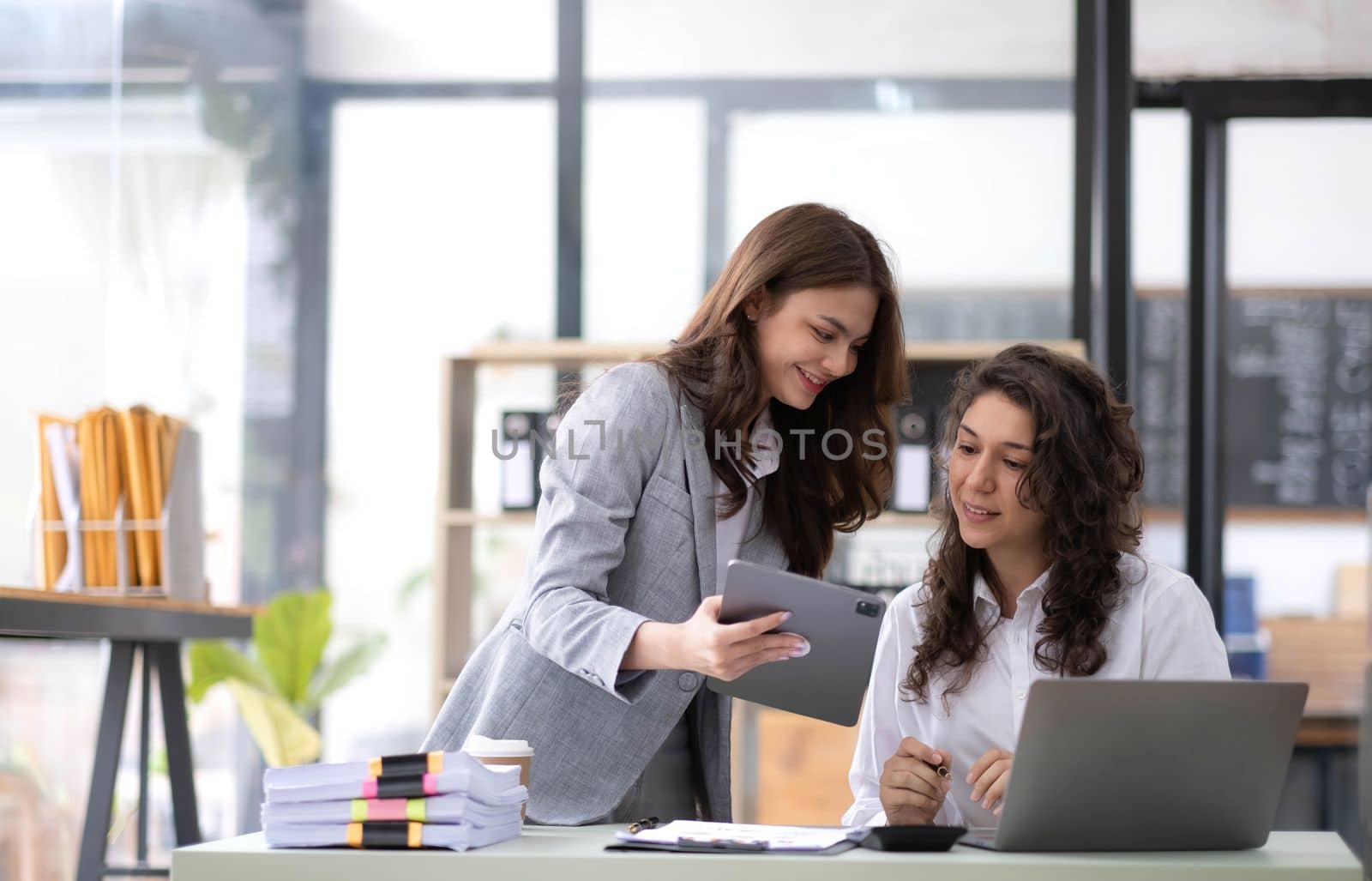 Two young Asian business woman talk, consult, discuss working with new startup project idea presentation analyze plan marketing and investment in the office..