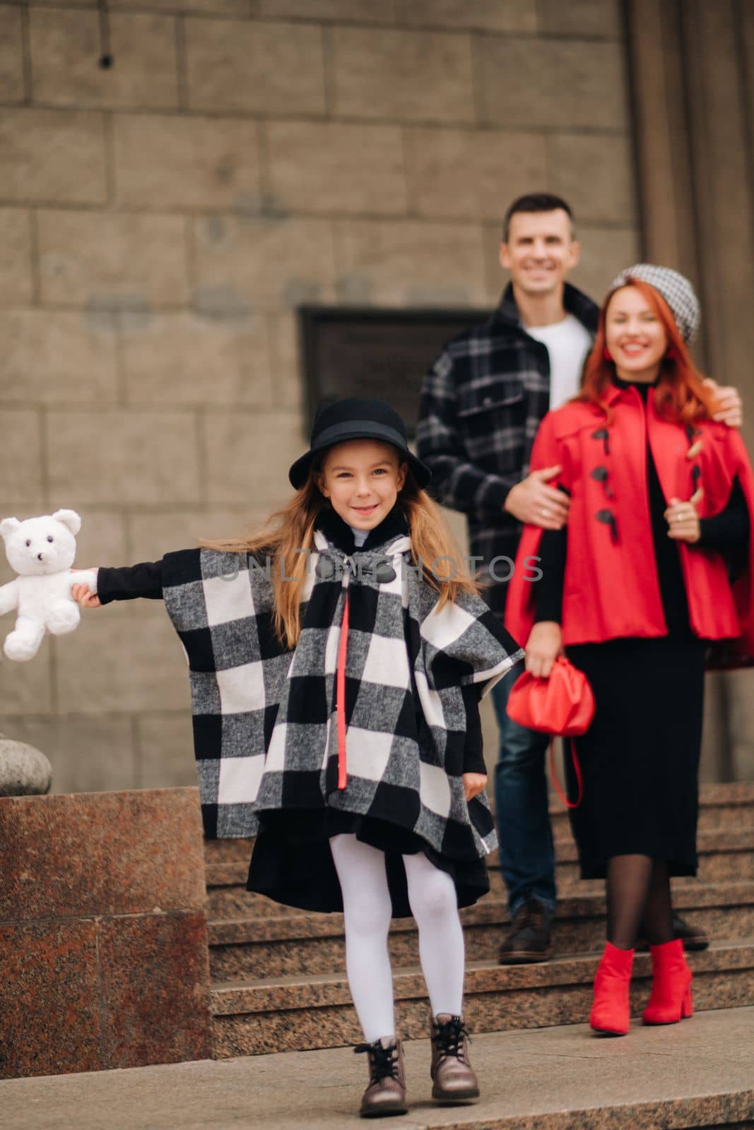 A stylish family of three is in town in the fall, and the girl with the stuffed toy is cheerful.