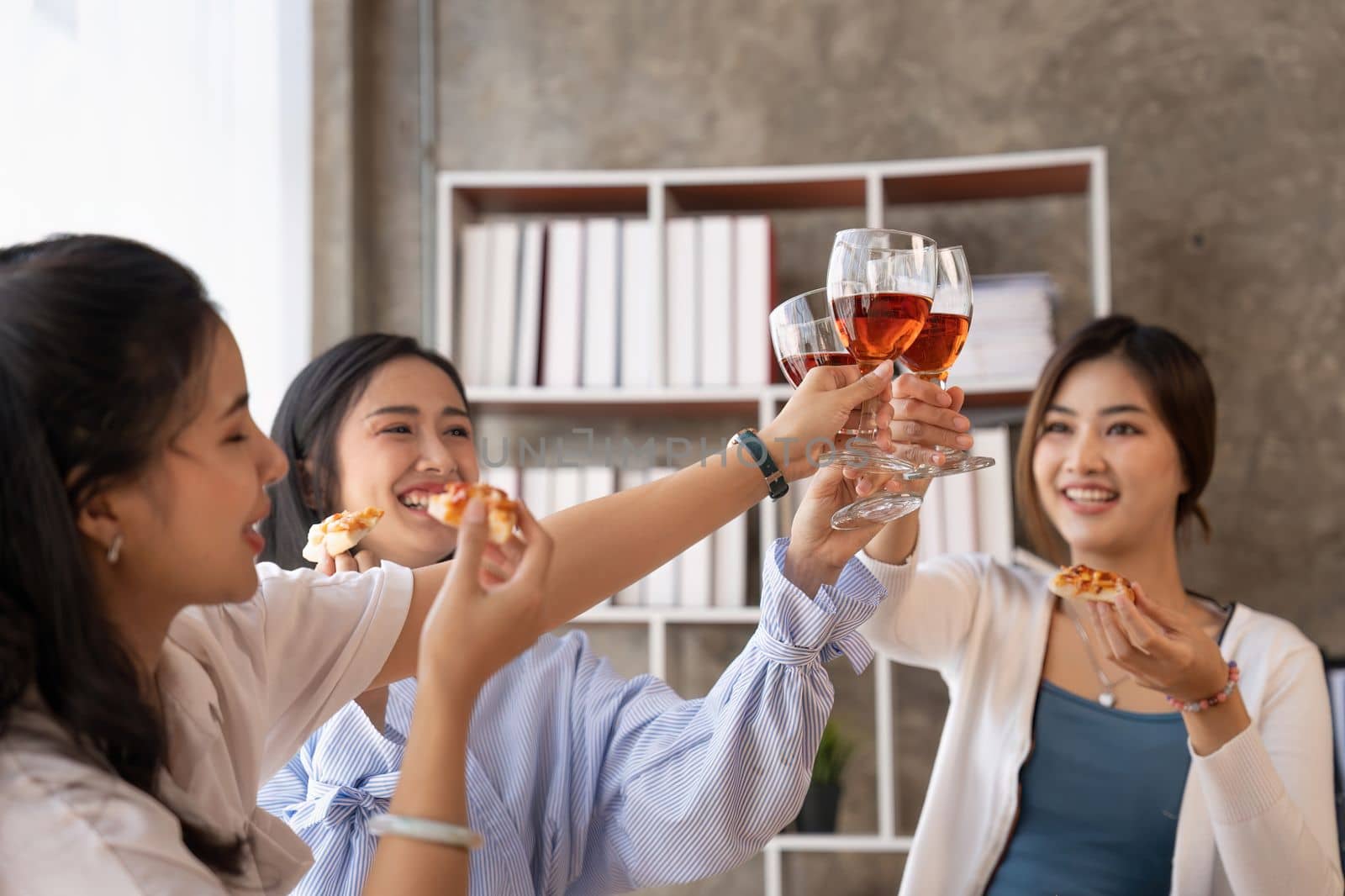 Group of Asian friends gather to celebrate Christmas with champagne and eating pizza at home. Joy of holiday party with friends or colleague concept.