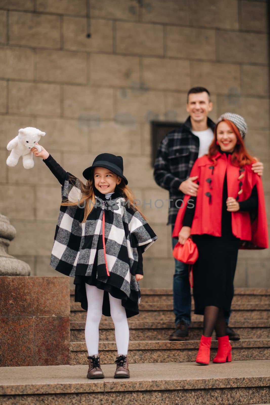 A stylish family of three is in town in the fall, and the girl with the stuffed toy is cheerful.