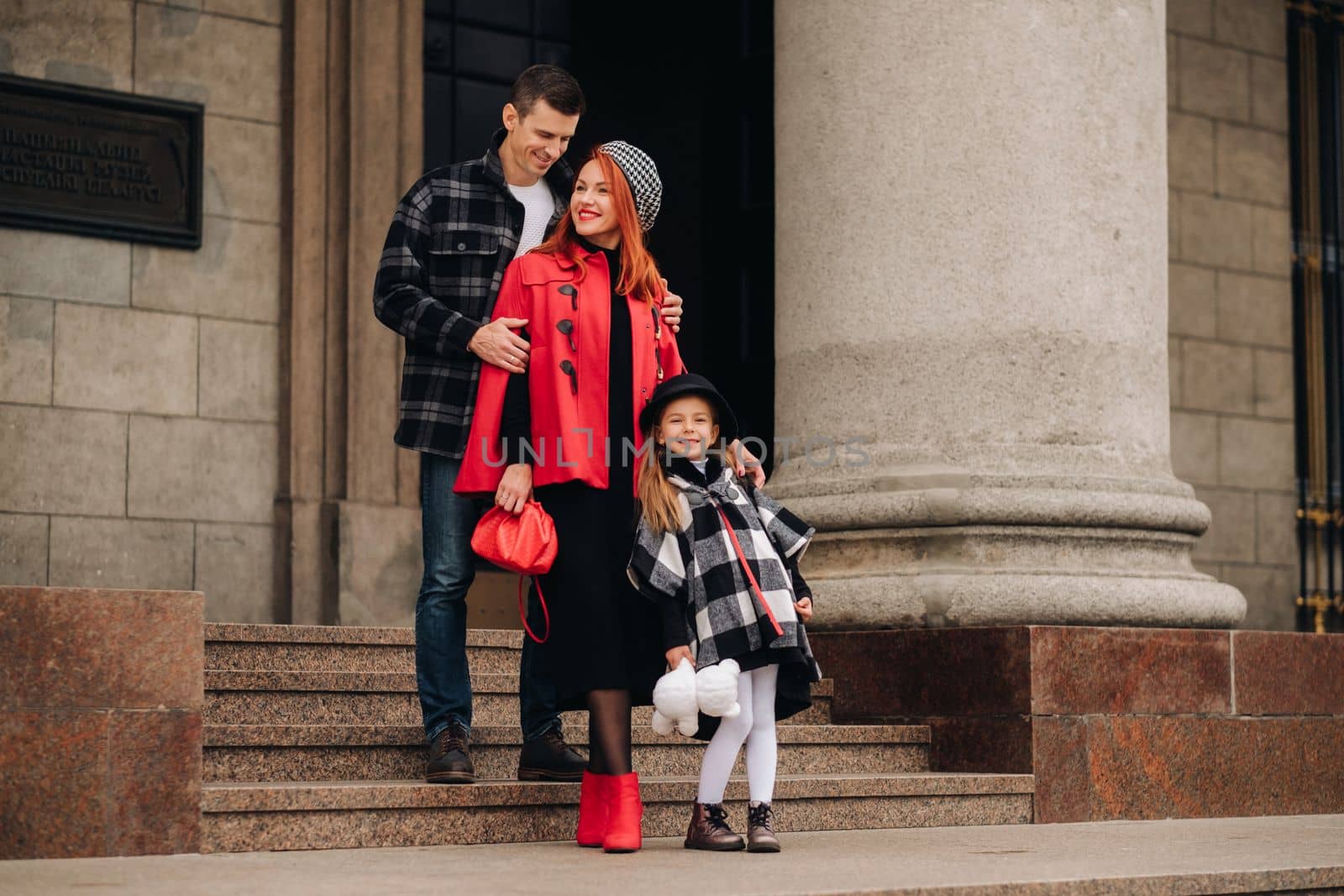 A stylish family of three strolls through the autumn city posing for a photographer . Dad, mom and daughter in the autumn city by Lobachad