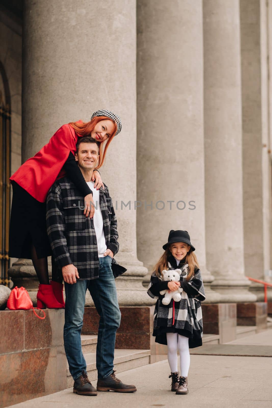 A stylish family of three strolls through the autumn city posing for a photographer . Dad, mom and daughter in the autumn city.