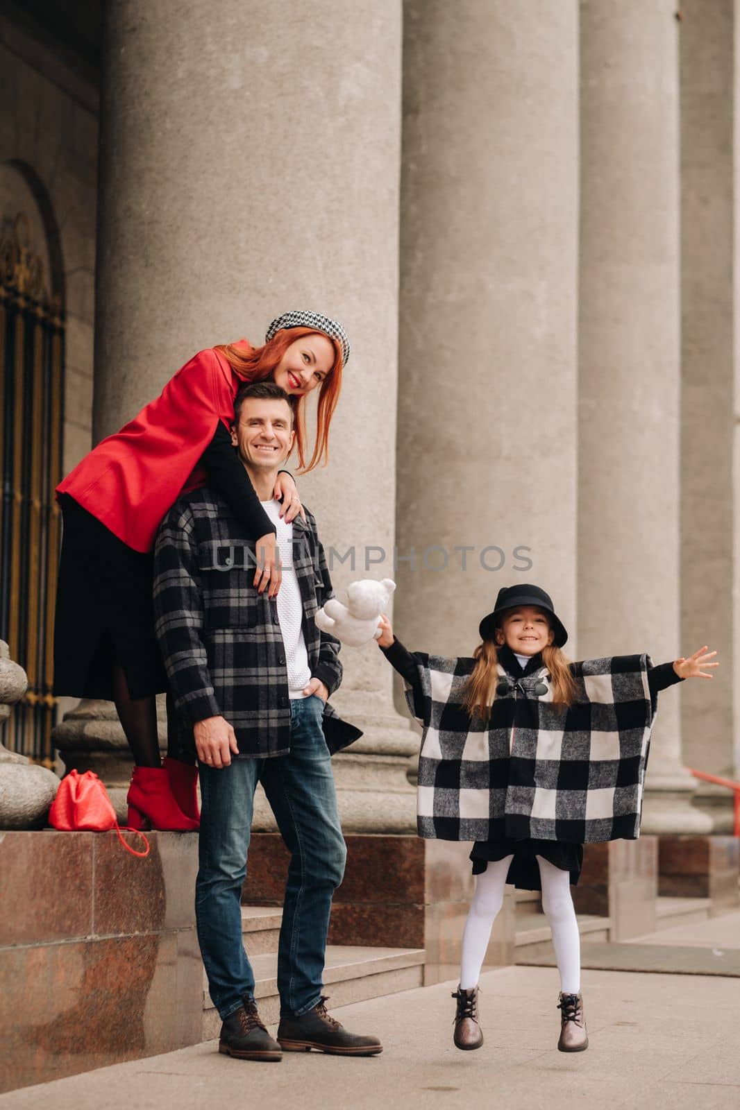 A stylish family of three strolls through the autumn city posing for a photographer . Dad, mom and daughter in the autumn city.