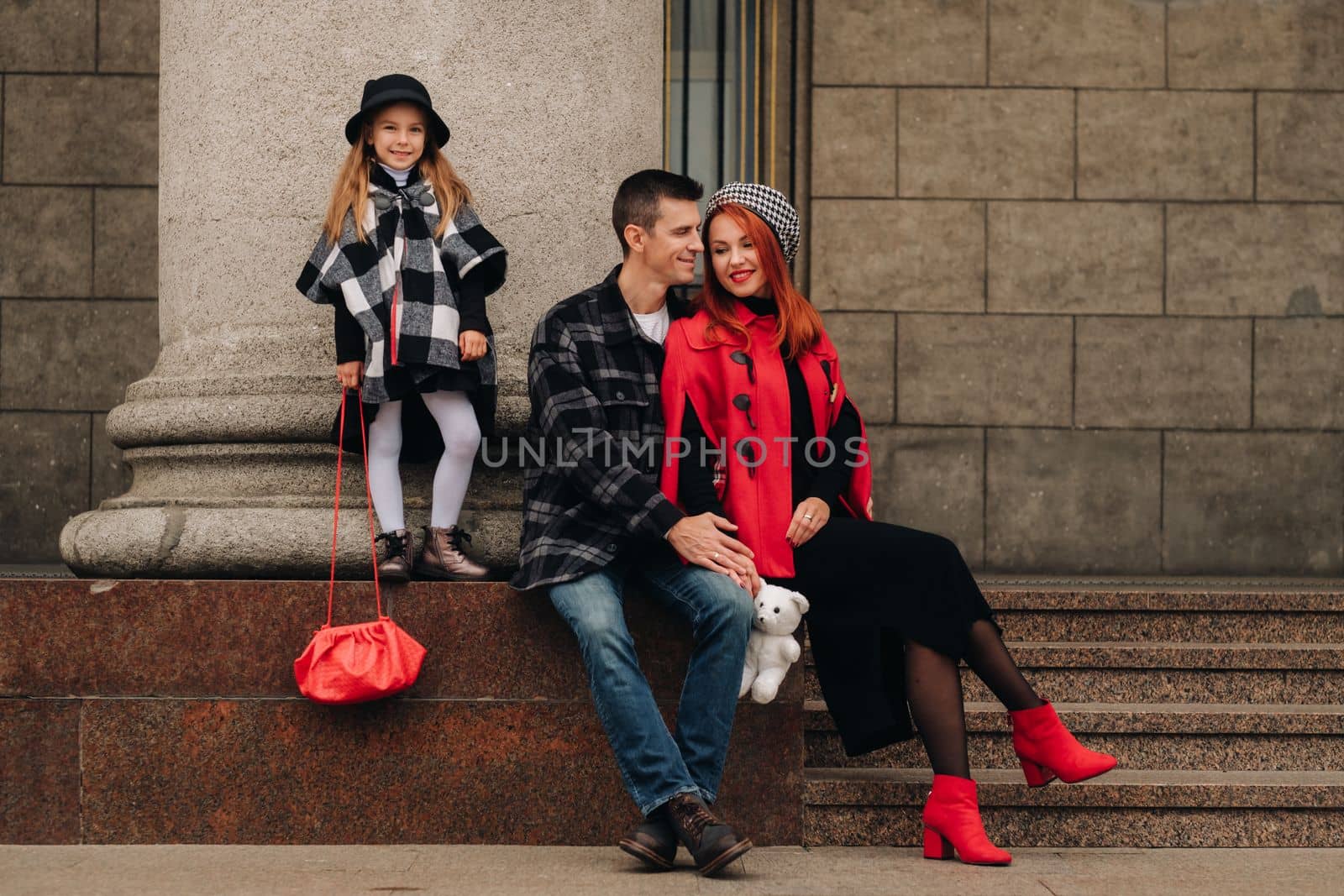 A stylish family of three strolls through the autumn city posing for a photographer . Dad, mom and daughter in the autumn city.