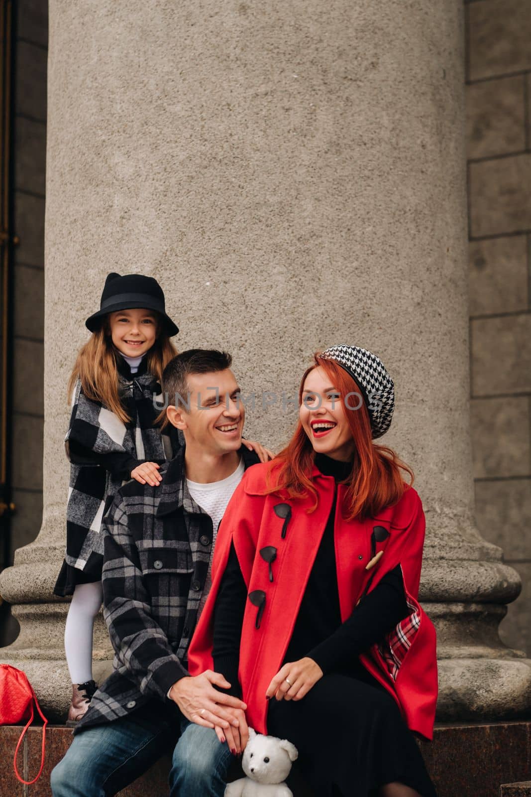 A stylish family of three strolls through the autumn city posing for a photographer . Dad, mom and daughter in the autumn city.