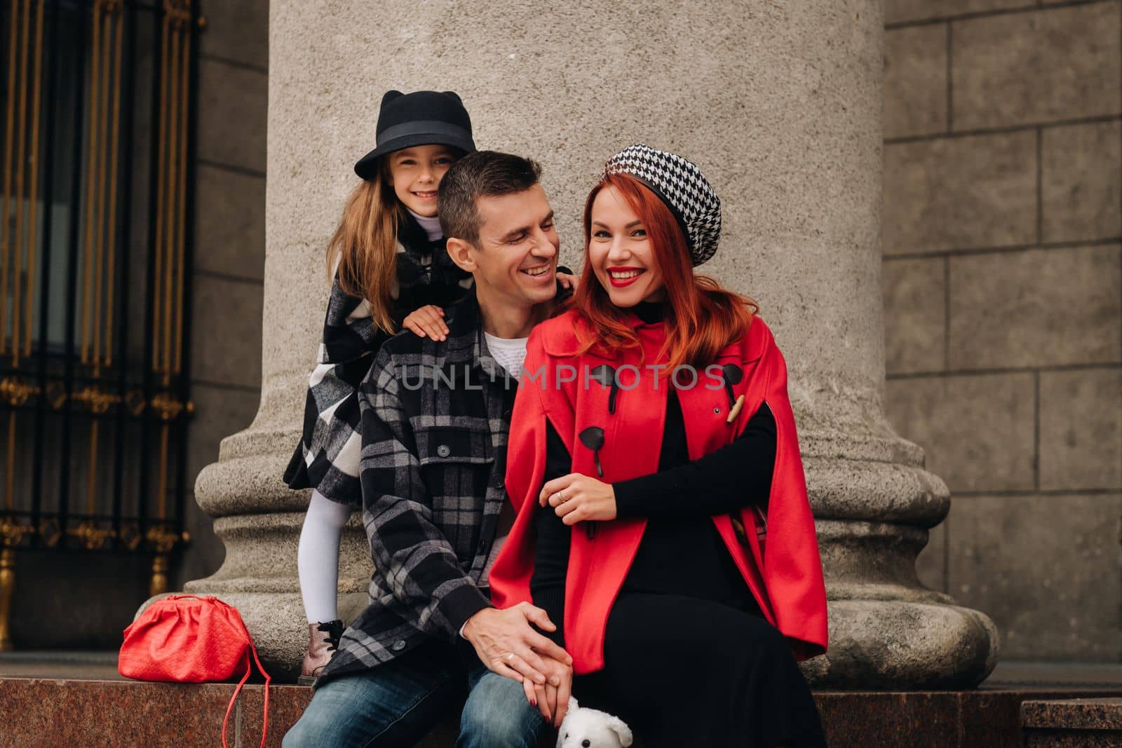 A stylish family of three strolls through the autumn city posing for a photographer . Dad, mom and daughter in the autumn city.