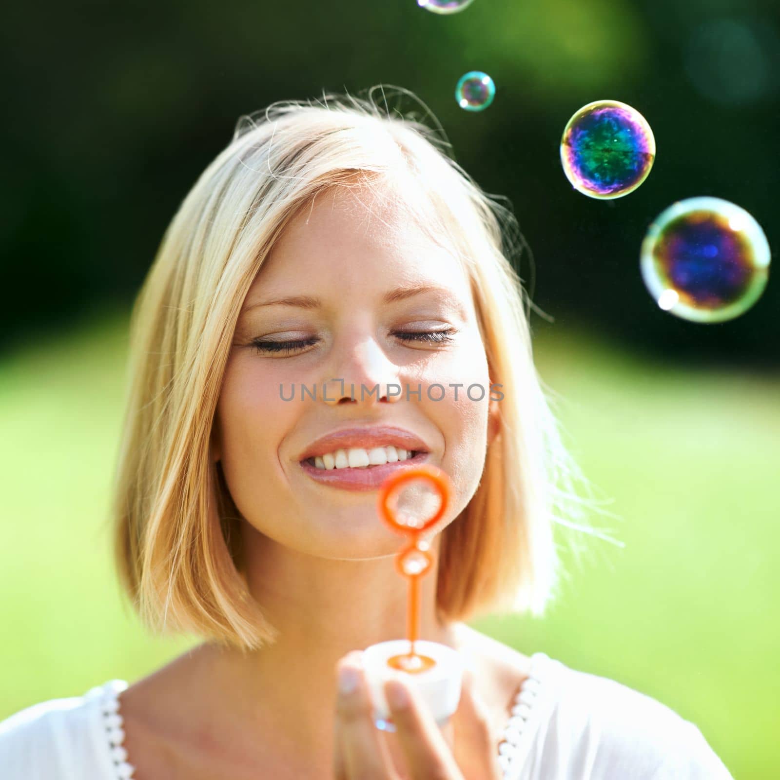 Having some innocent fun. Smiling young woman blowing soap bubbles outdoors. by YuriArcurs