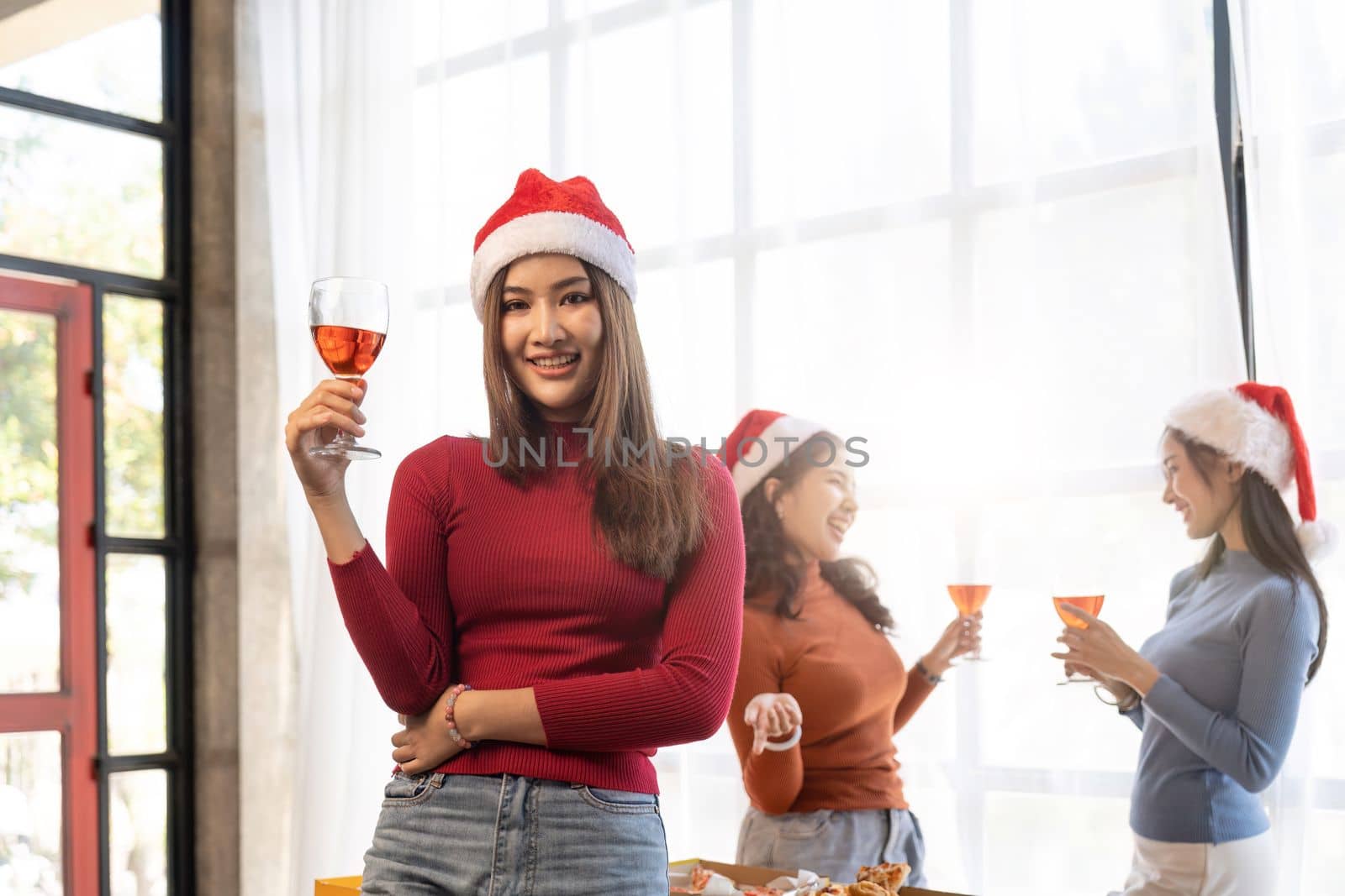 Group of Asian friends gather to celebrate Christmas with champagne and eating pizza at home. Joy of holiday party with friends or colleague concept.