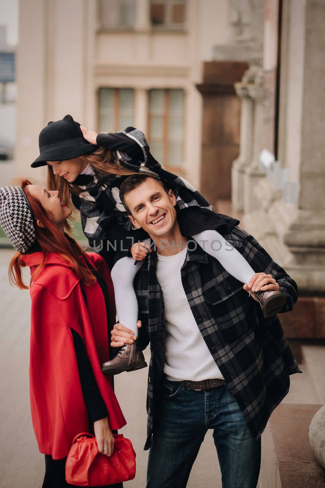 A stylish family of three strolls through the autumn city posing for a photographer . Dad, mom and daughter in the autumn city.