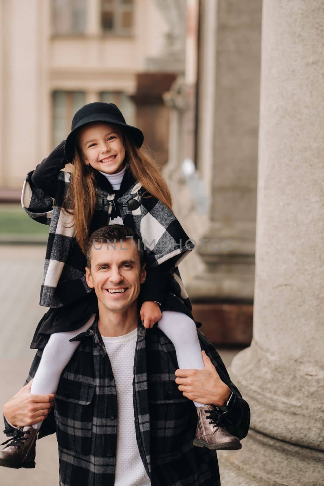 A cheerful Daughter is sitting on dad's shoulders and walking around the autumn city.