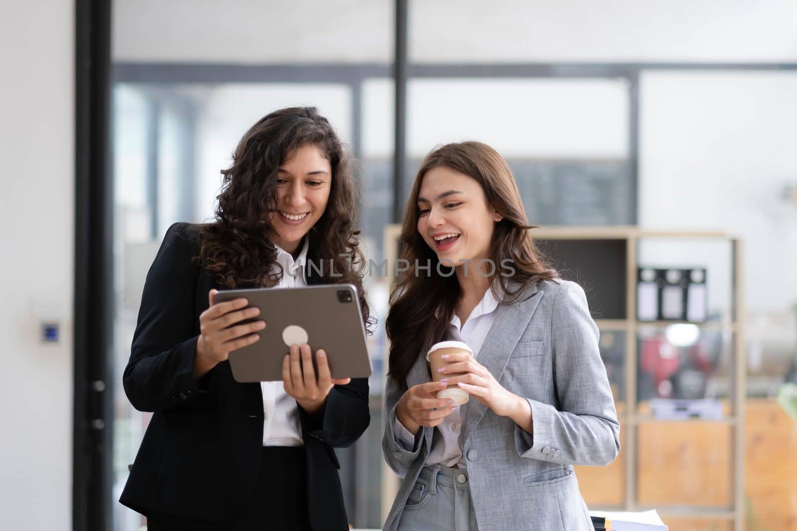 Two beautiful Asian businesswomen standing using digital tablet consulting and analyzing information in office work. by wichayada