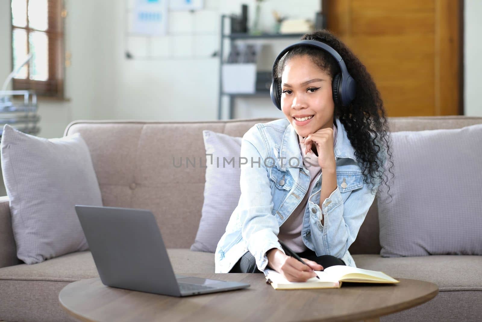 Smiling Asian young female using headphones looking at laptop screen listen and learning online courses