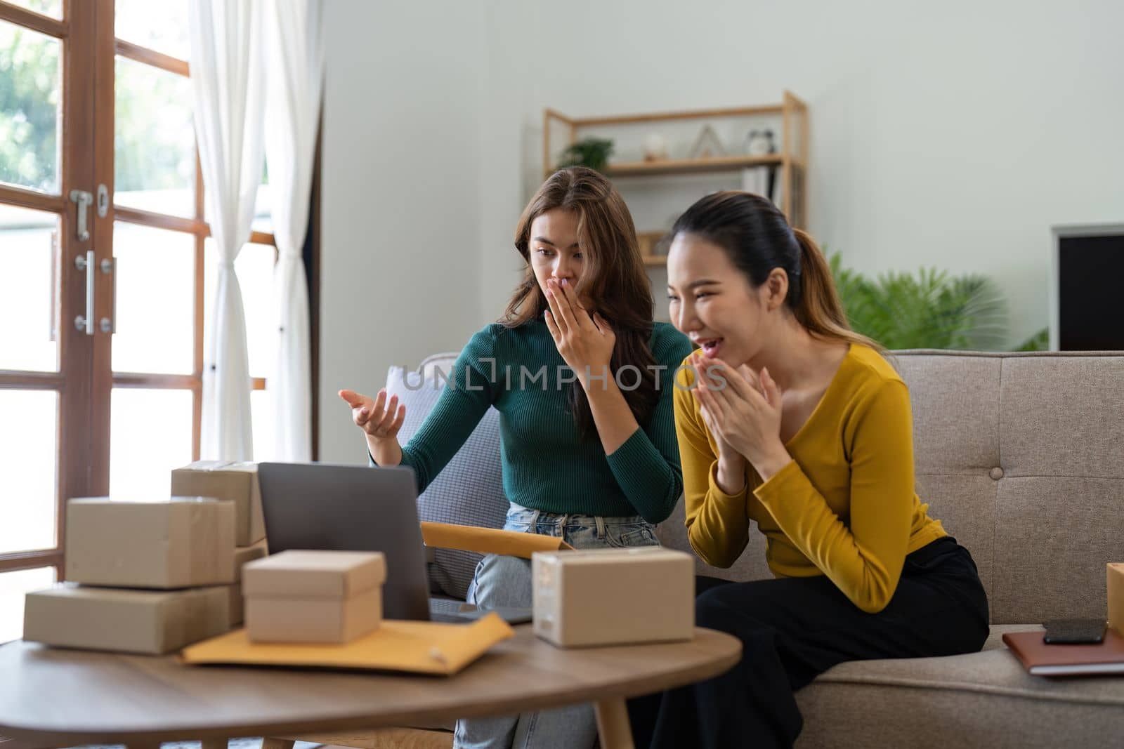 Two Young Asian women are happy and excited after a new order from SME customer, commercial checking, online marketing, Entrepreneur packing boxes, SME sellers, and freelance online sales concept.