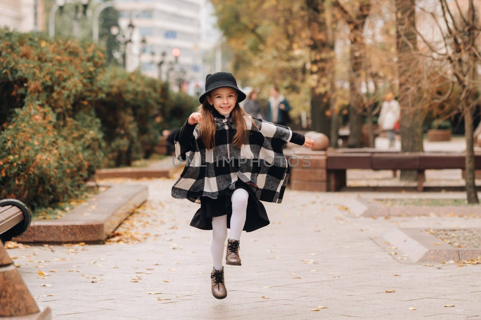 A stylish little girl in a hat walks around the autumn city.
