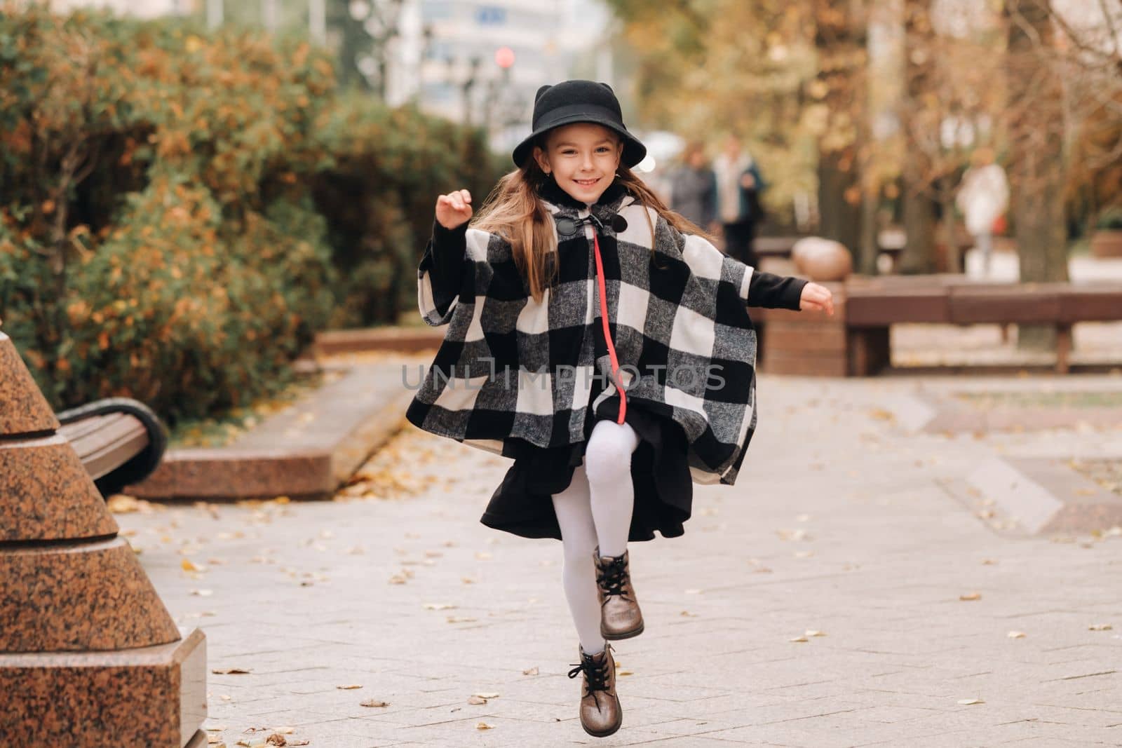 A stylish little girl in a hat walks around the autumn city.