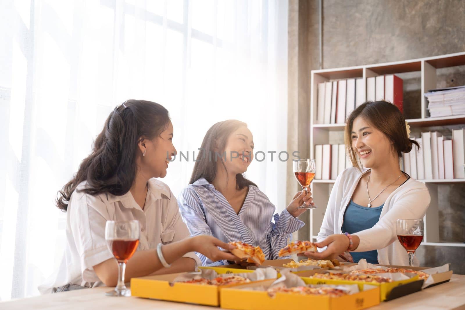 Group of Asian friends gather to celebrate Christmas with champagne and eating pizza at home. Joy of holiday party with friends or colleague concept.