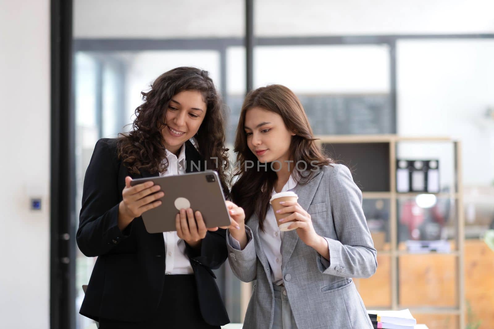 Two beautiful Asian businesswomen standing using digital tablet consulting and analyzing information in office work. by wichayada