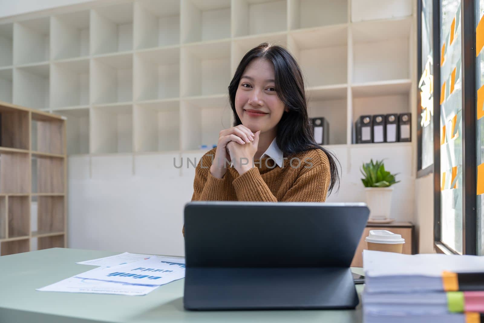 Portrait of Young beautiful Asian businesswoman sitting and smiling while working on laptop, Looking at camera by nateemee