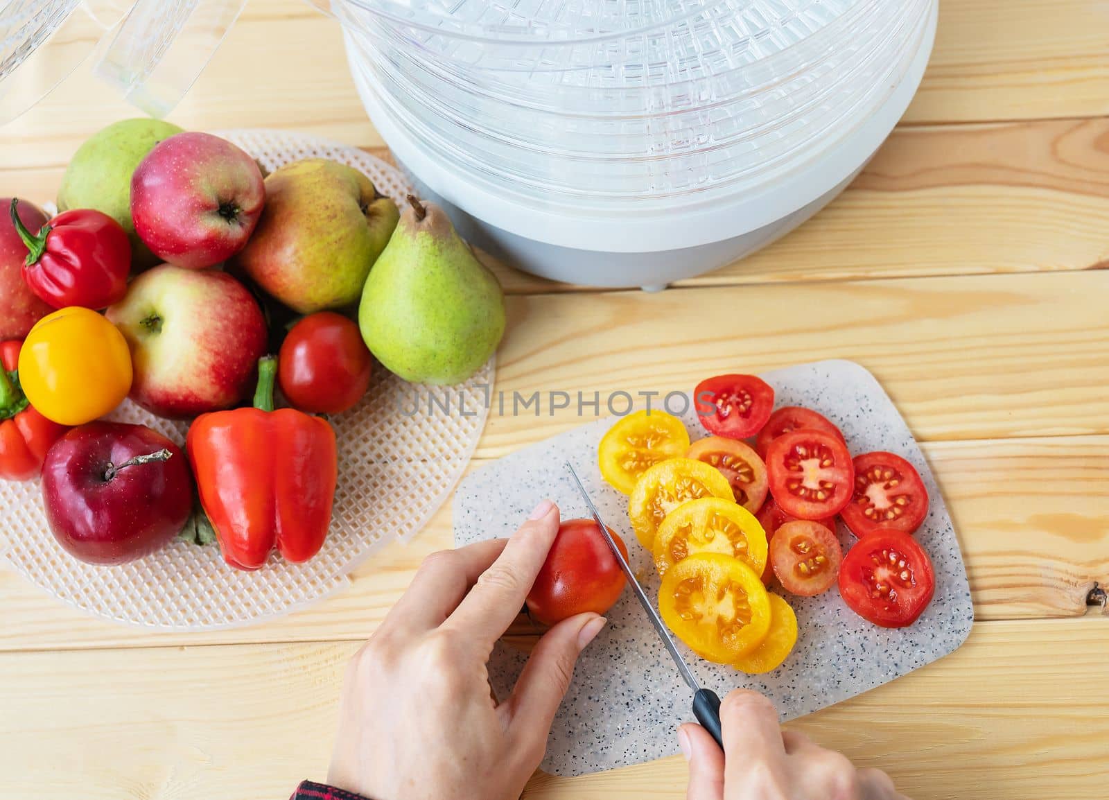 Electric drying machine for dehydrating products with horizontal loading of pallets. Top view, girl cuts tomatoes for drying, close-up, natural light