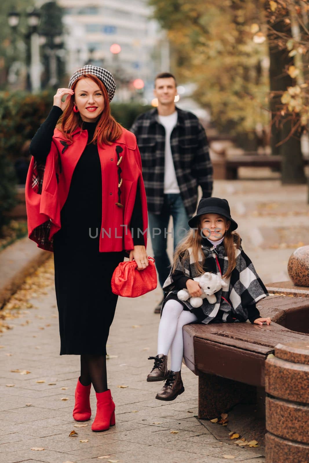 A stylish family of three strolls through the autumn city posing for a photographer . Dad, mom and daughter in the autumn city by Lobachad