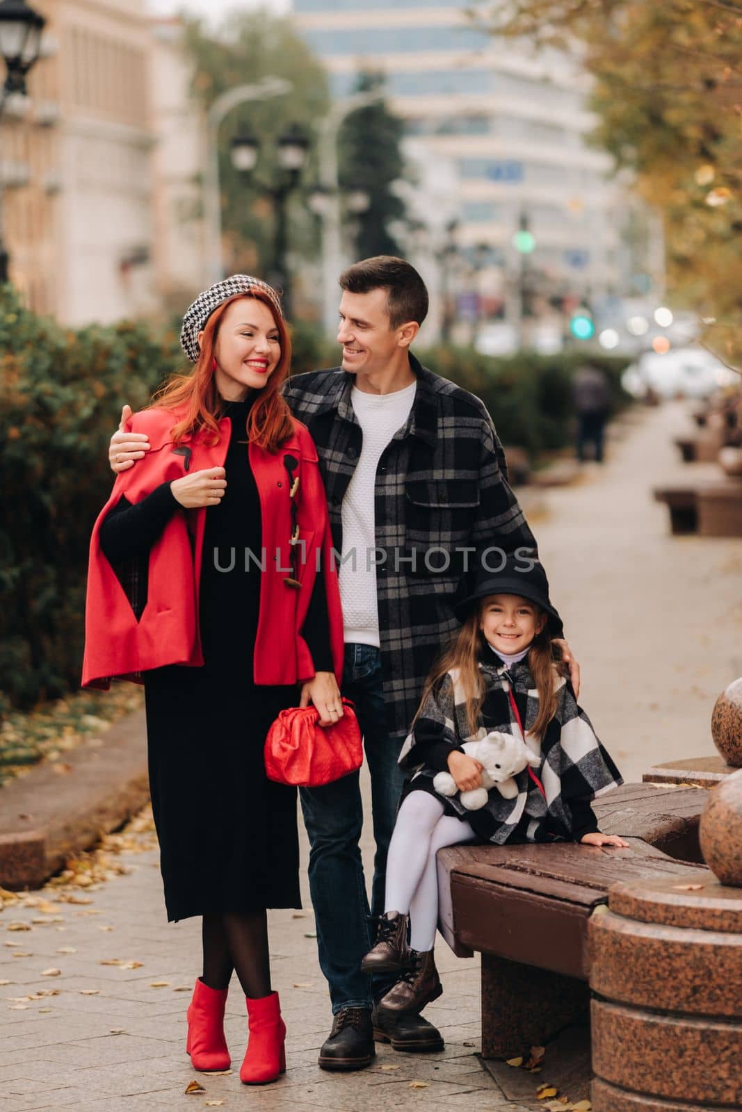 A stylish family of three strolls through the autumn city posing for a photographer . Dad, mom and daughter in the autumn city by Lobachad