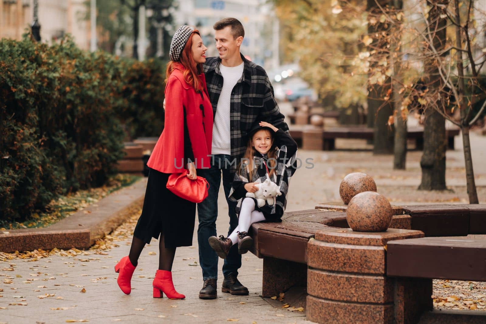 A stylish family of three strolls through the autumn city posing for a photographer . Dad, mom and daughter in the autumn city by Lobachad