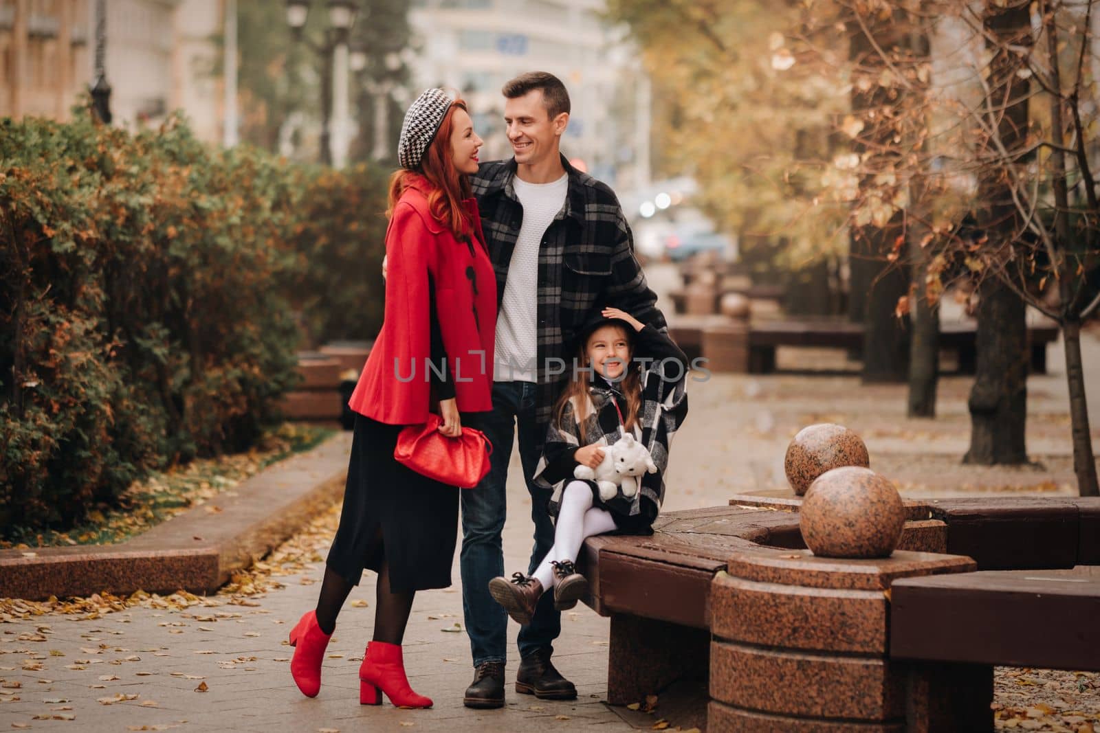 A stylish family of three strolls through the autumn city posing for a photographer . Dad, mom and daughter in the autumn city by Lobachad