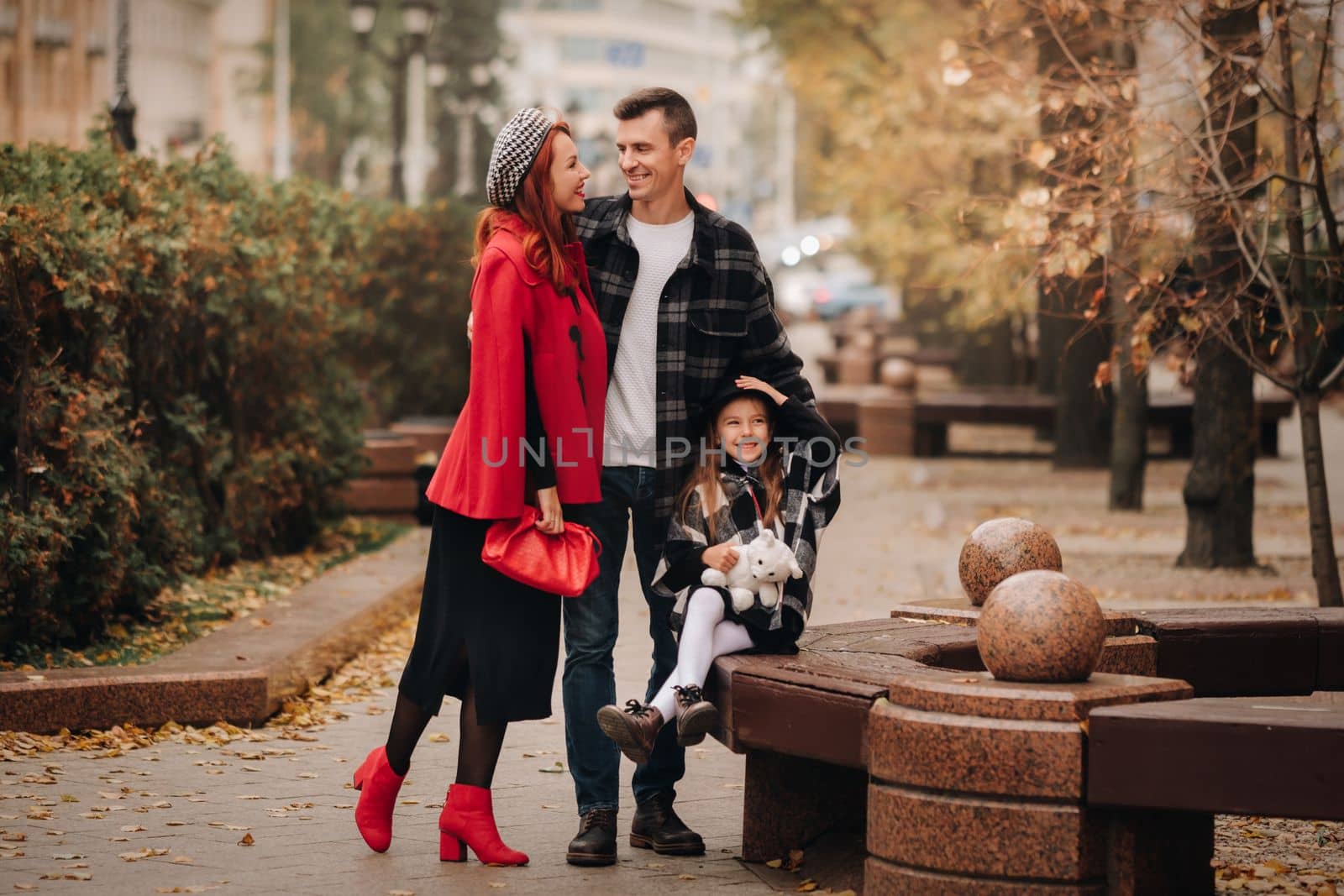 A stylish family of three strolls through the autumn city posing for a photographer . Dad, mom and daughter in the autumn city.