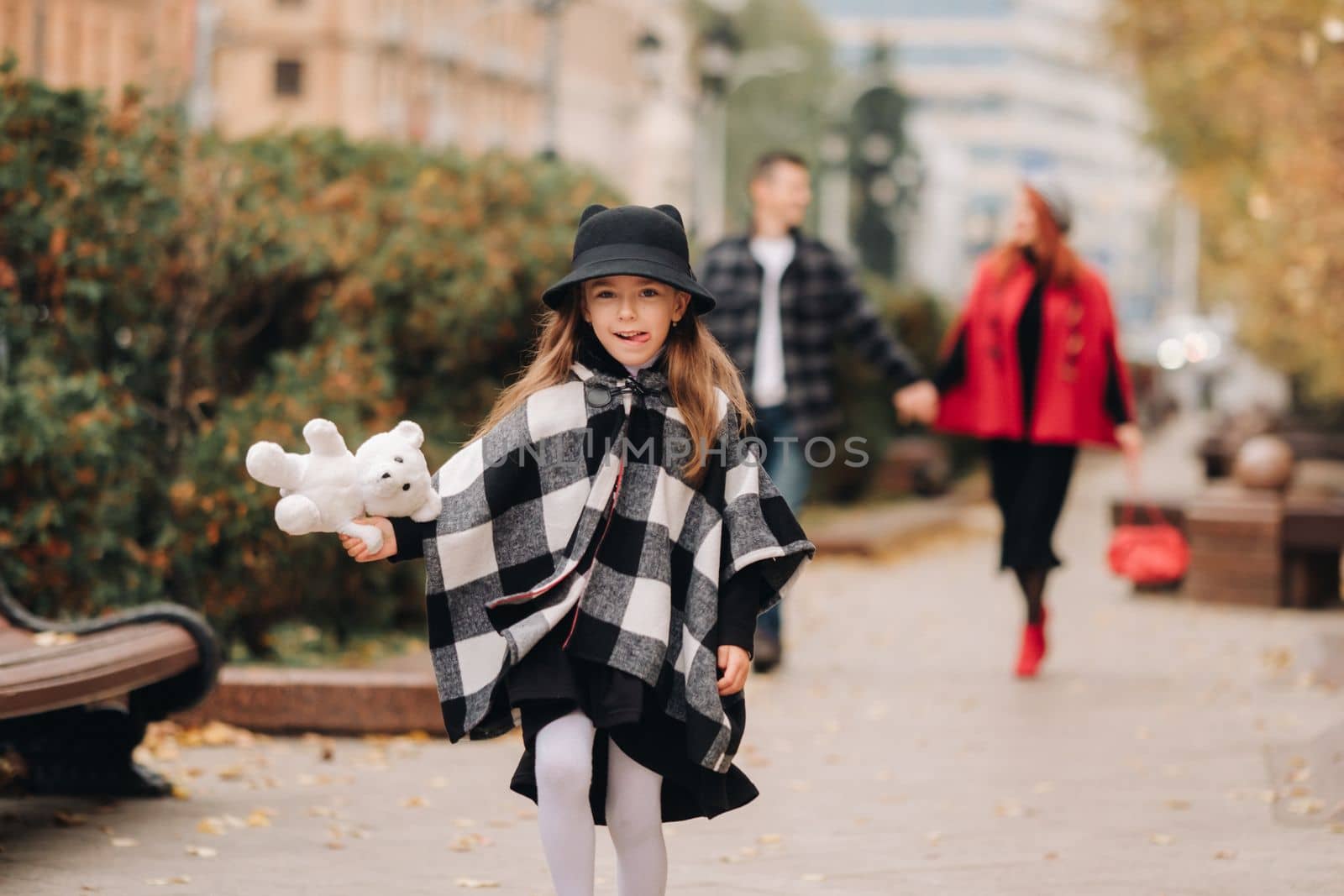 A little girl with her parents runs to the autumn city.A stylish family of three strolls through the autumn city by Lobachad