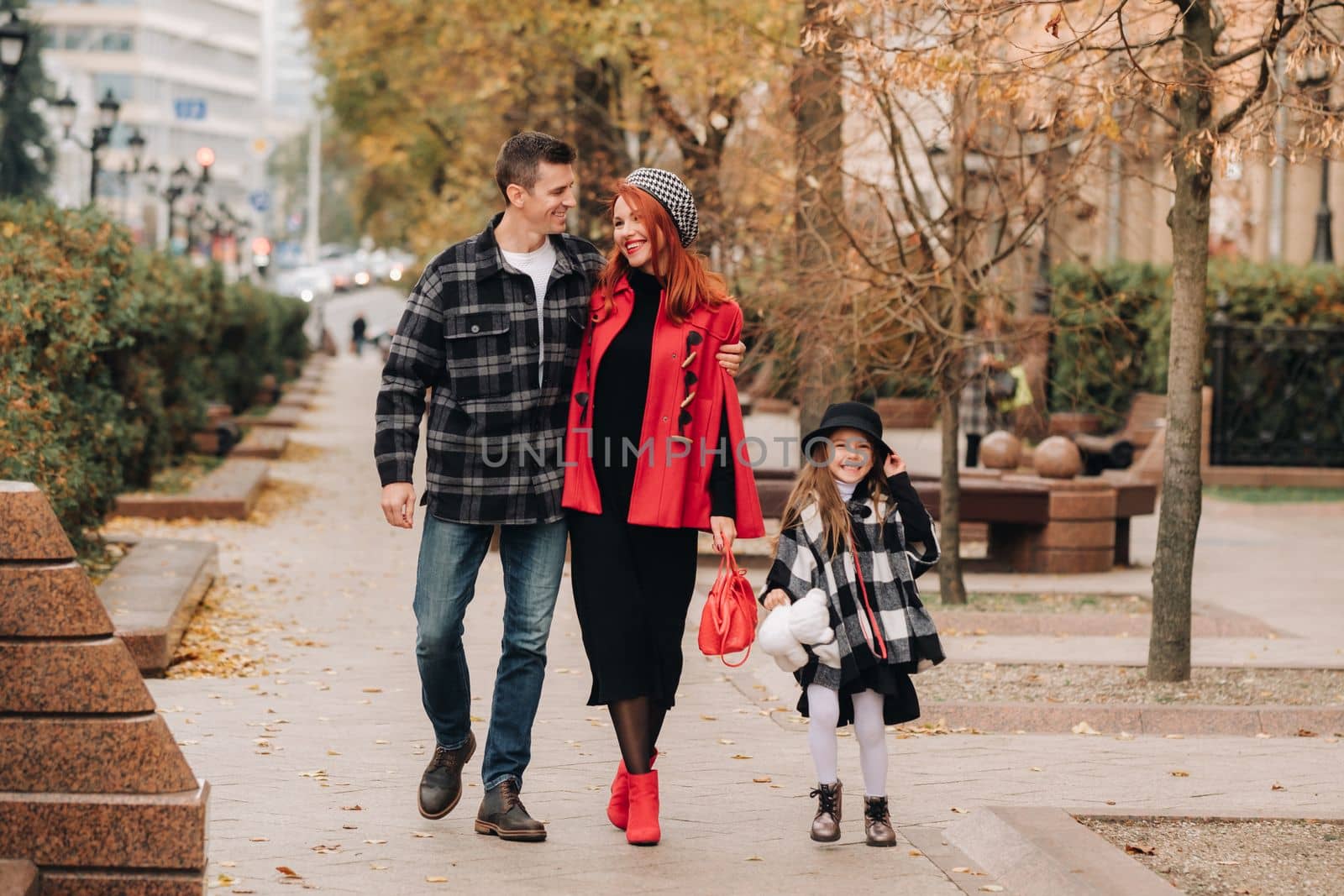 A little girl with her parents runs to the autumn city.A stylish family of three strolls through the autumn city,