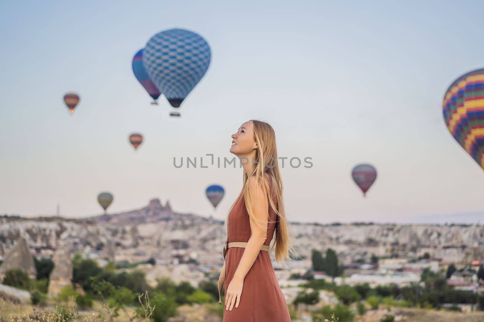 Tourist woman looking at hot air balloons in Cappadocia, Turkey. Happy Travel in Turkey concept. Woman on a mountain top enjoying wonderful view.