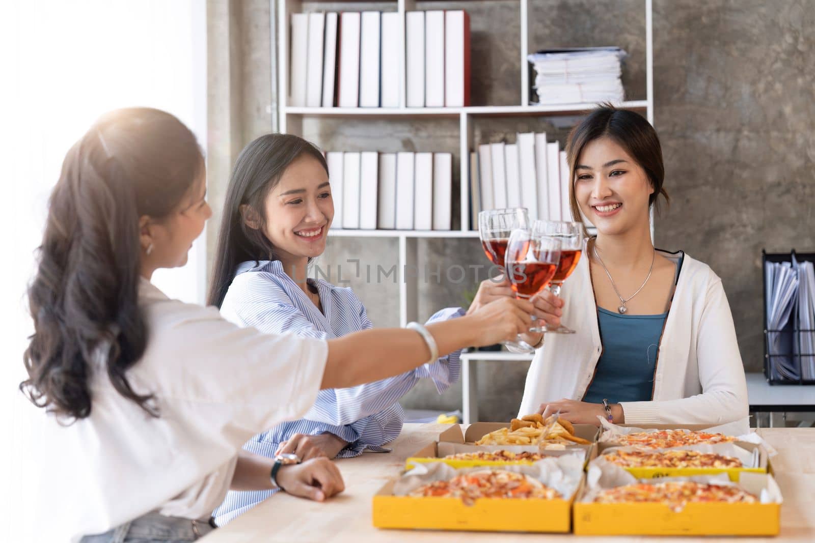 Group of Asian friends gather to celebrate Christmas with champagne and eating pizza at home. Joy of holiday party with friends or colleague concept.