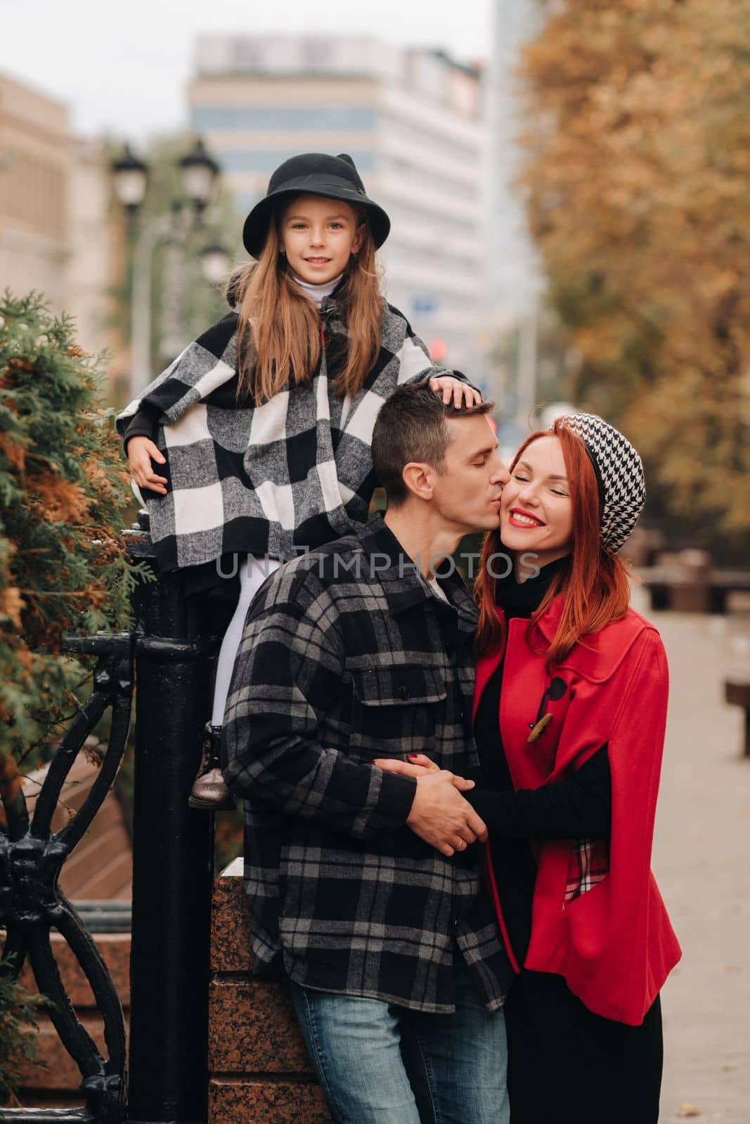 A stylish family of three strolls through the autumn city posing for a photographer . Dad, mom and daughter in the autumn city.