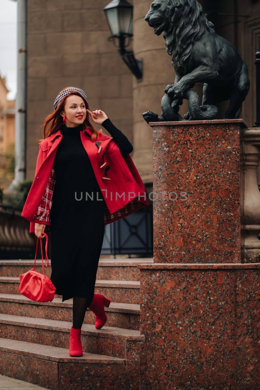 A beautiful stylish woman dressed in an elegant red coat with a stylish red handbag in the autumn city.