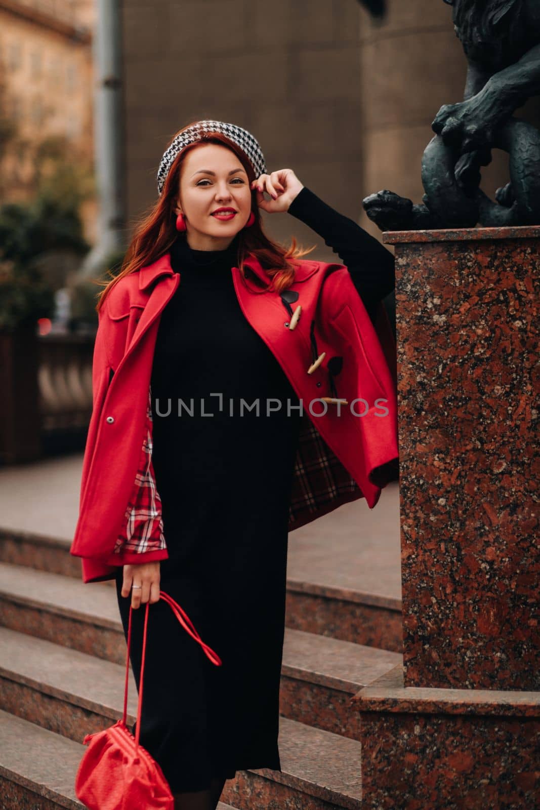 A beautiful stylish woman dressed in an elegant red coat with a stylish red handbag in the autumn city by Lobachad