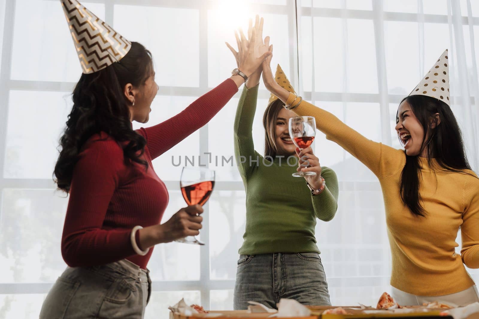 Group of Asian friends gather to celebrate Christmas with champagne and eating pizza at home. Joy of holiday party with friends or colleague concept.