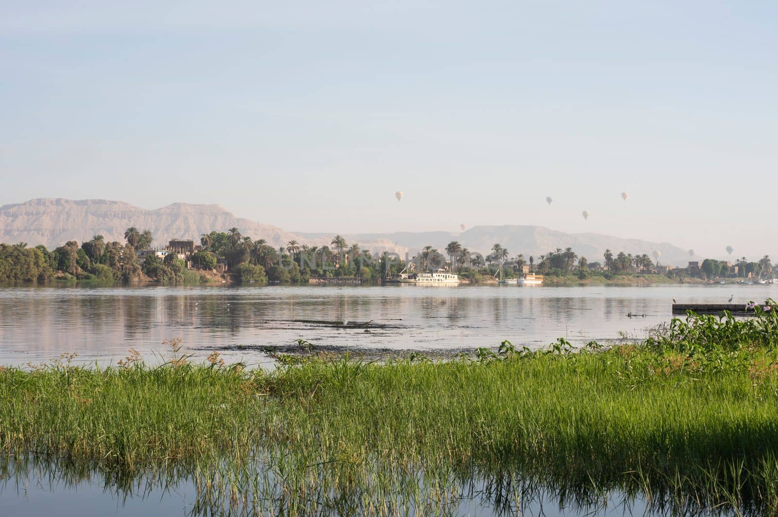 Panoramic landscape view across nile river to luxor west bank with mountains and hot air balloons flying