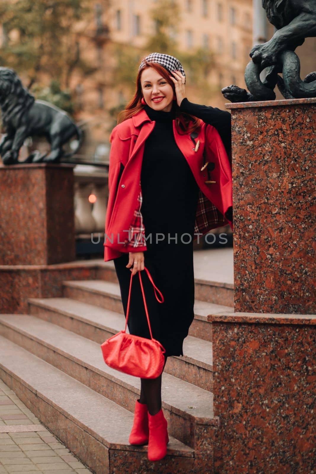 A beautiful stylish woman dressed in an elegant red coat with a stylish red handbag in the autumn city.