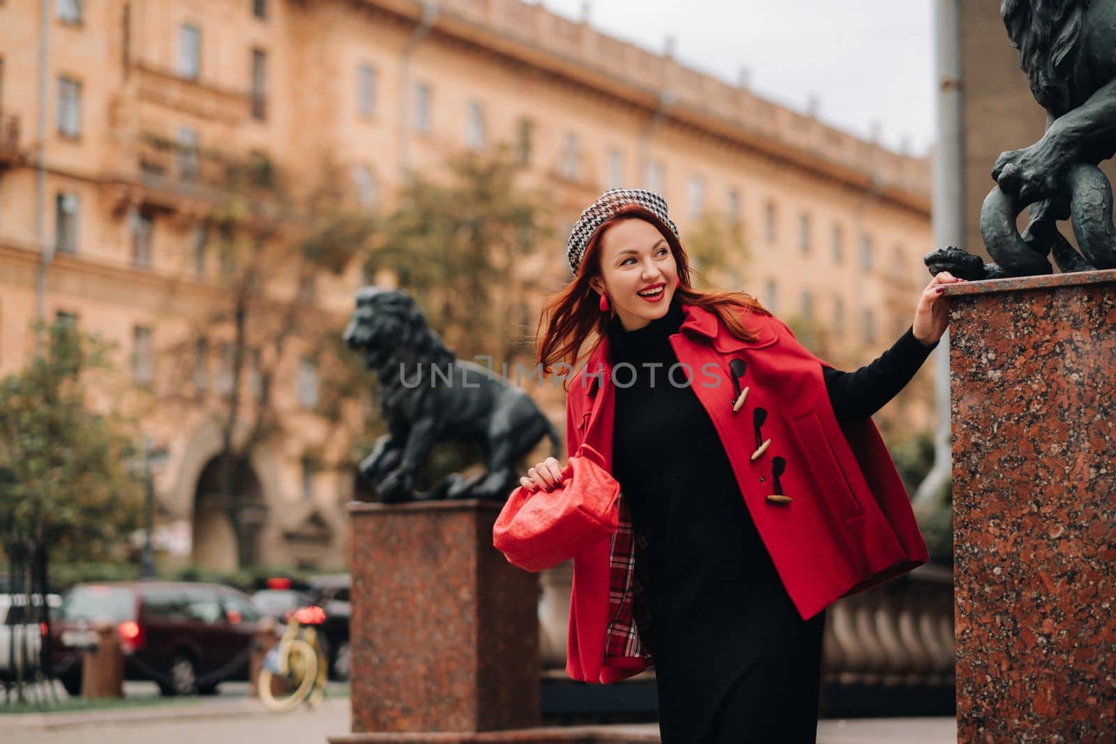 A beautiful stylish woman dressed in an elegant red coat with a stylish red handbag in the autumn city by Lobachad