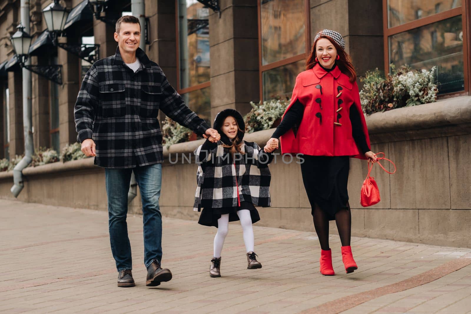 A stylish family of three walks in the city in autumn holding hands.
