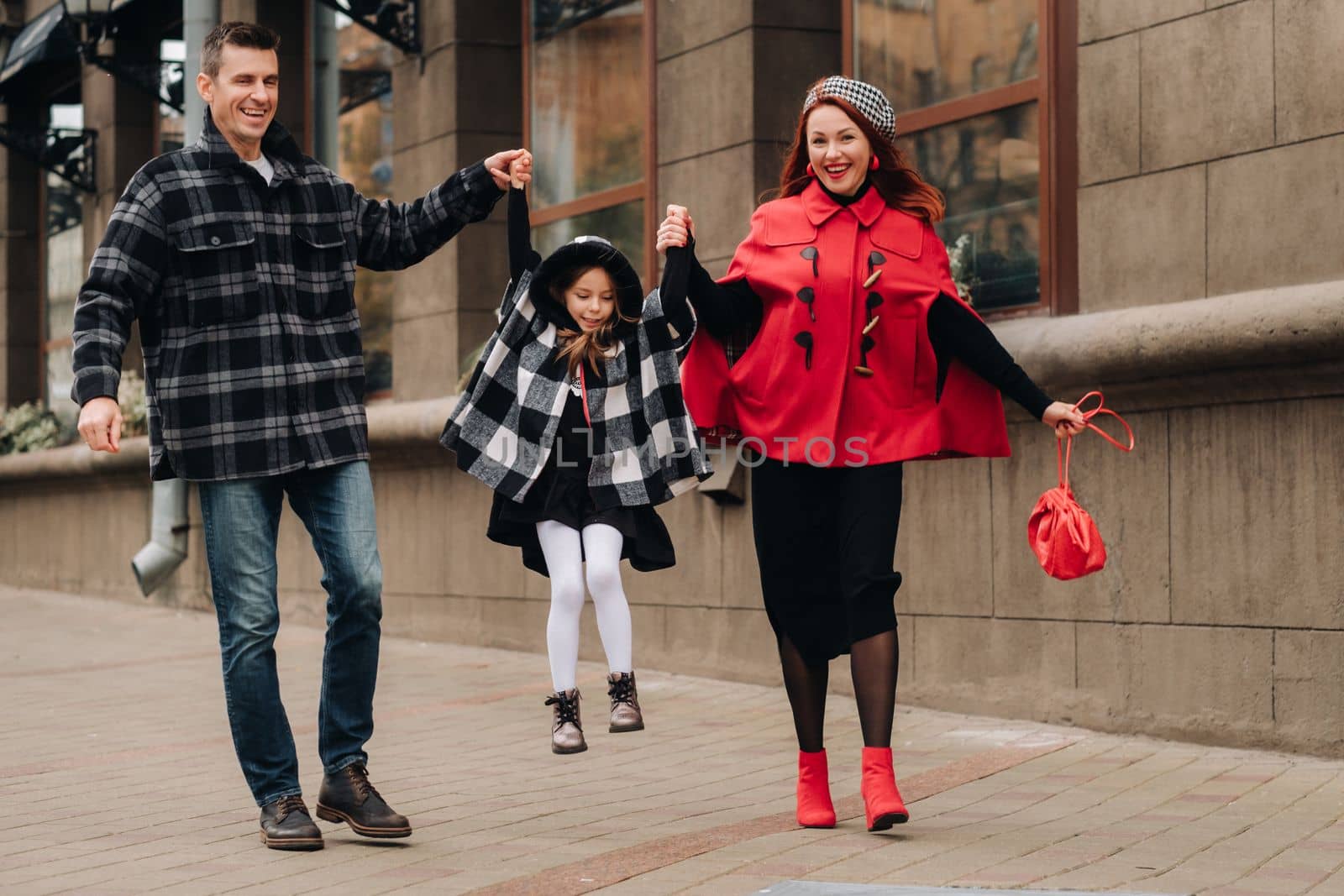 A stylish family of three walks in the city in autumn holding hands.