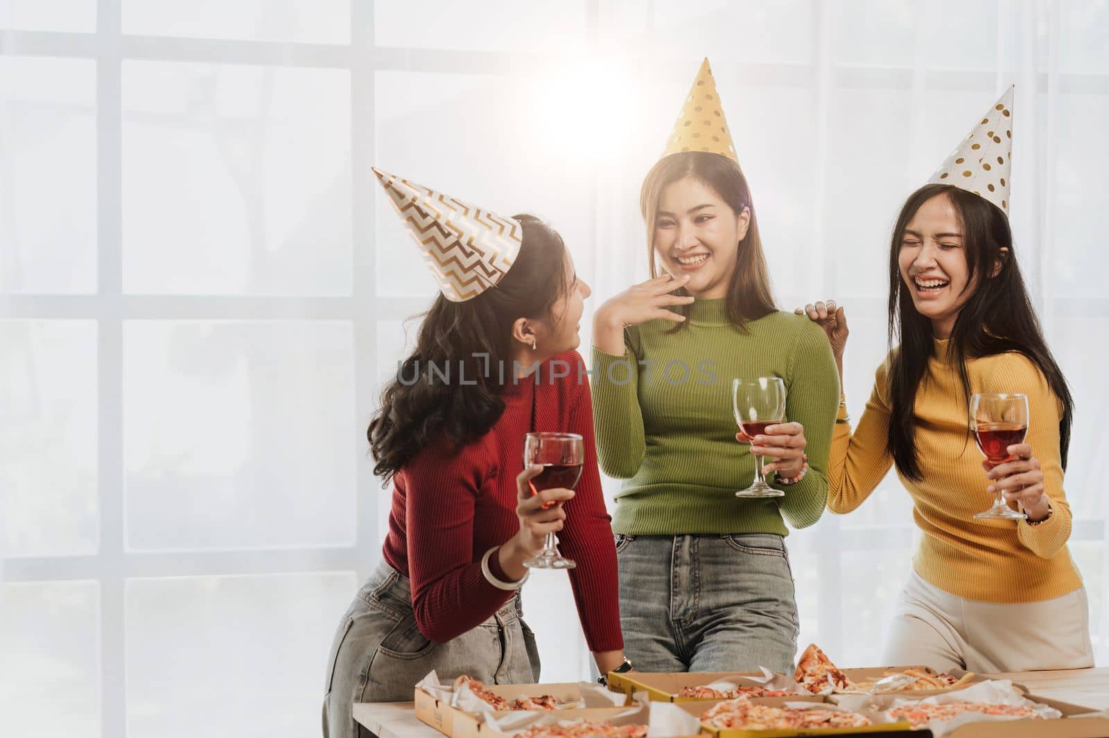 Group of Asian friends gather to celebrate Christmas with champagne and eating pizza at home. Joy of holiday party with friends or colleague concept by nateemee
